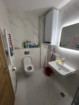 Modern bathroom with light tiles, a washbasin, and a toilet. - image 14