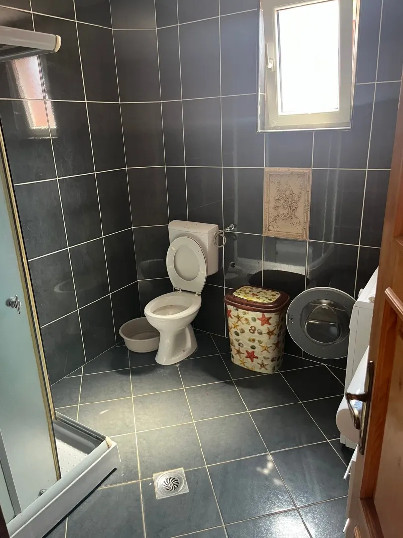Kupatilo obloženo tamnim pločicama sa toaletom, tuš kabinom i veš mašinom.
