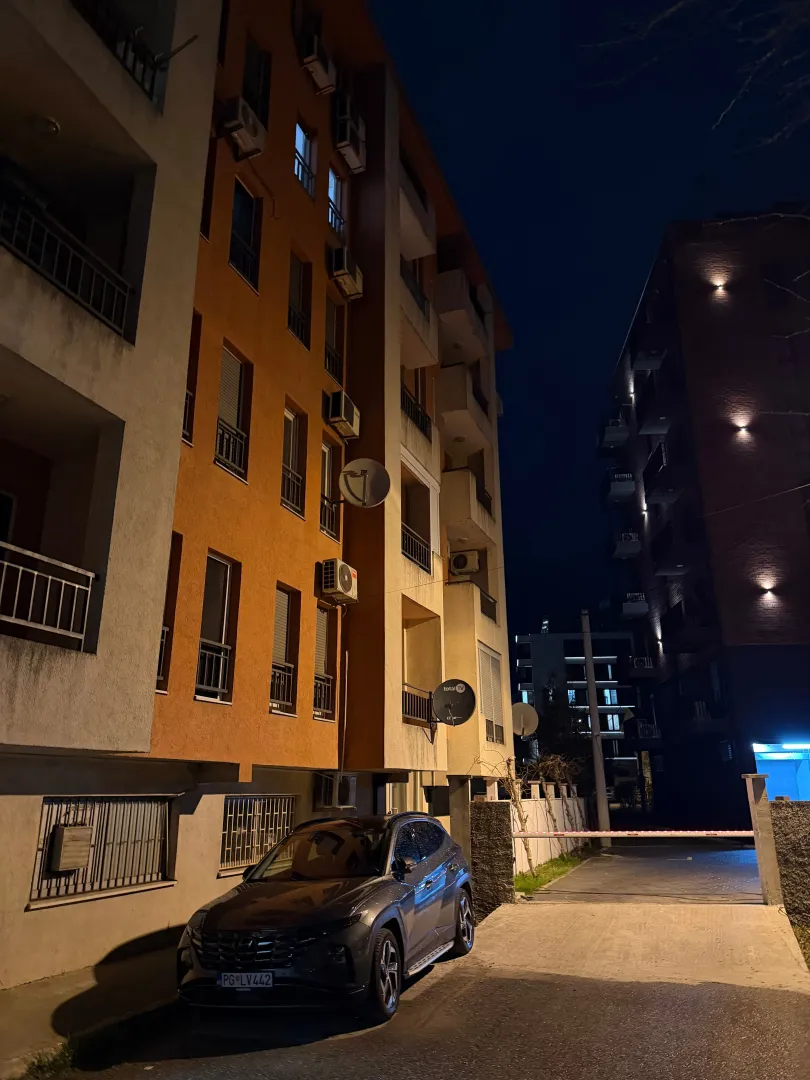 Pogled na spoljašnjost stambene zgrade sa parkingom noću.