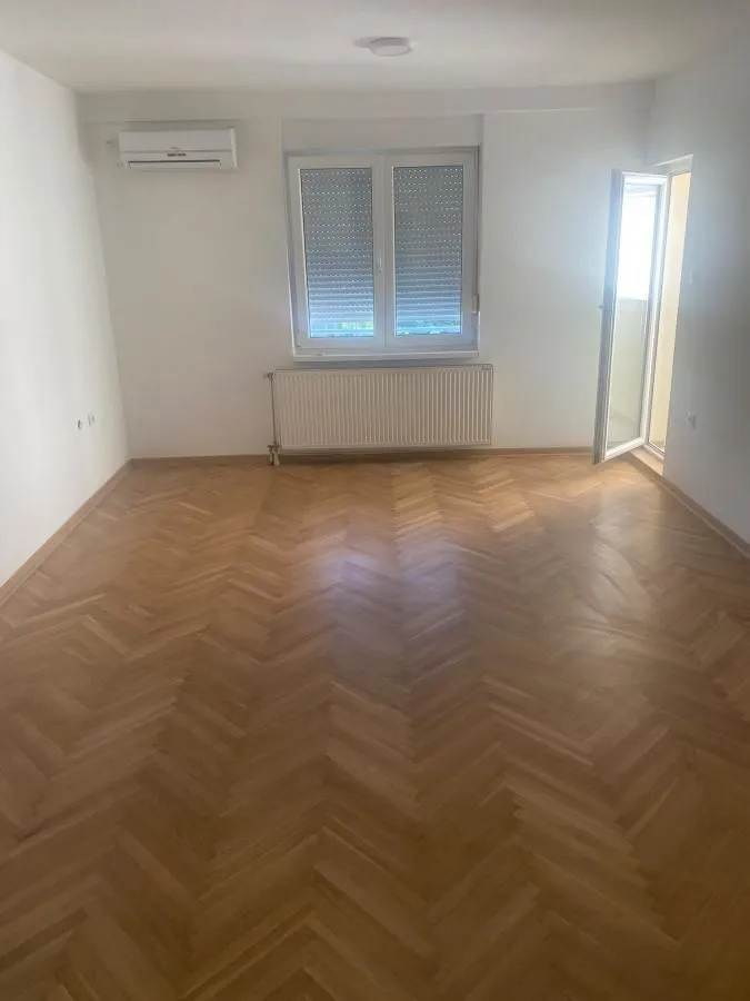 Prazna soba sa parketom, klima uređajem i prozorom.