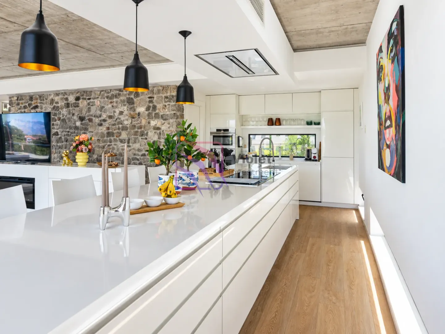 Modern kitchen with a large island, built-in appliances, and a stone wall accent.