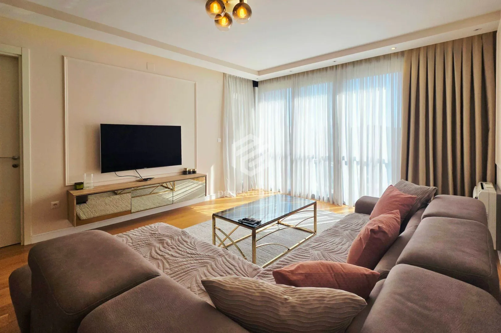 Spacious living room with a sectional sofa, TV, and large windows.