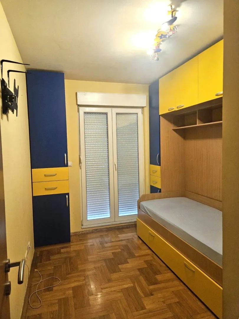 Children's bedroom with a bed, fitted wardrobes, and parquet flooring.