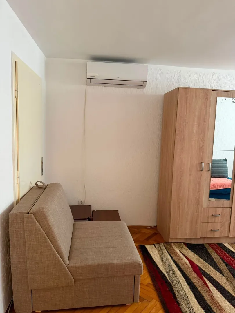 Manja spavaća soba sa krevetom na razvlačenje, drvenim ormarom i klima uređajem.