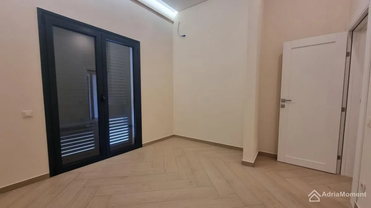 Prazna soba sa svijetlim laminatom i balkonskim vratima.