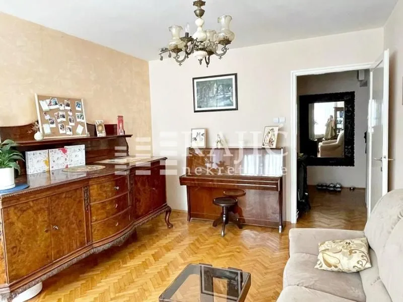 Living room with a sofa, sideboard, piano, and parquet flooring.