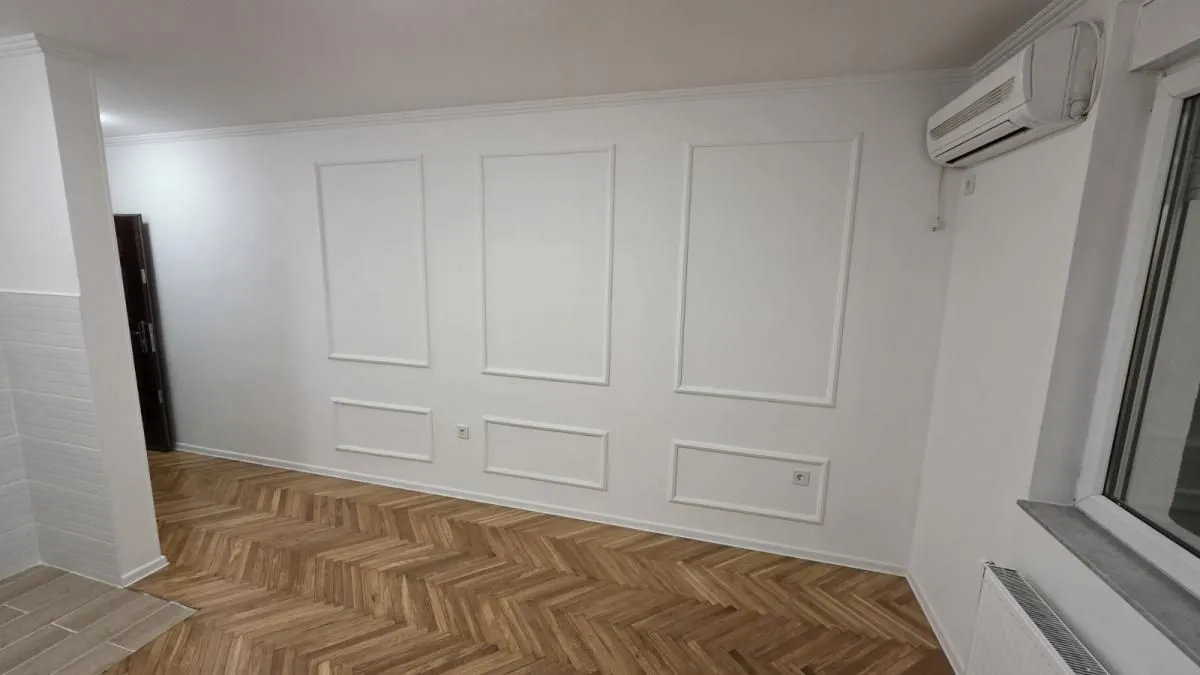 Prazna prostorija sa belim zidovima ukrašenim lajsnama i drvenim podom.