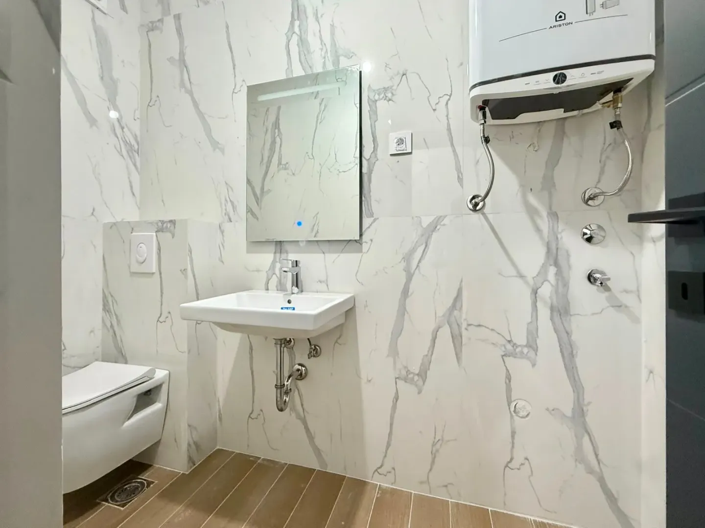 Moderne kupatilo obloženo mermernim pločicama sa umivaonikom i wc šoljom.