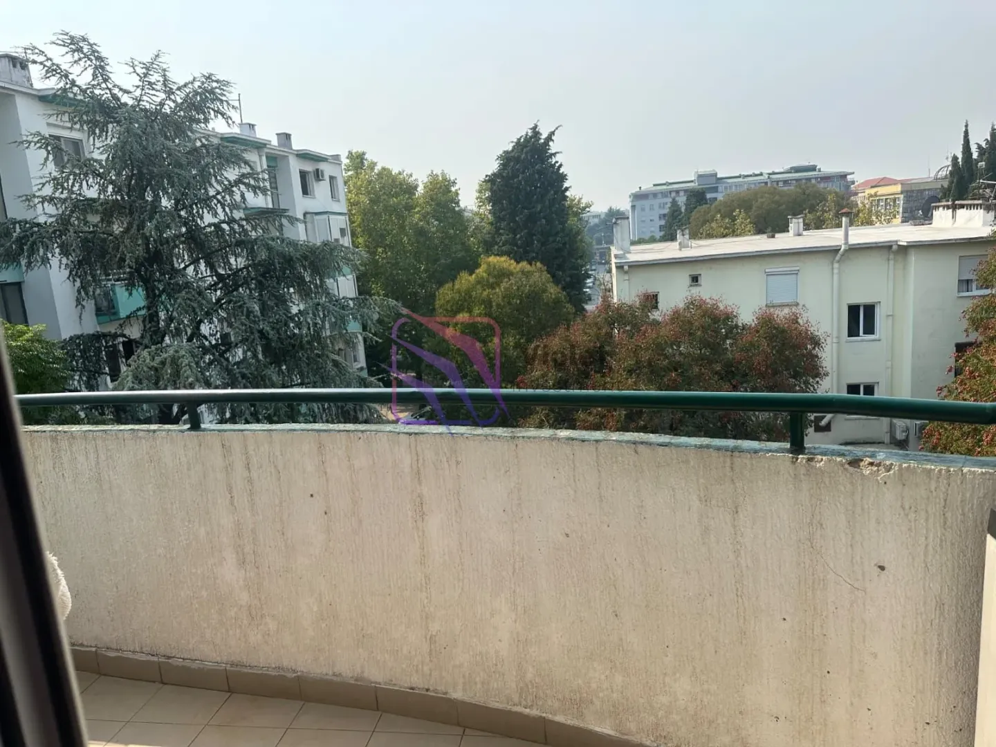 Pogled sa balkona na okolne zgrade i drveće.