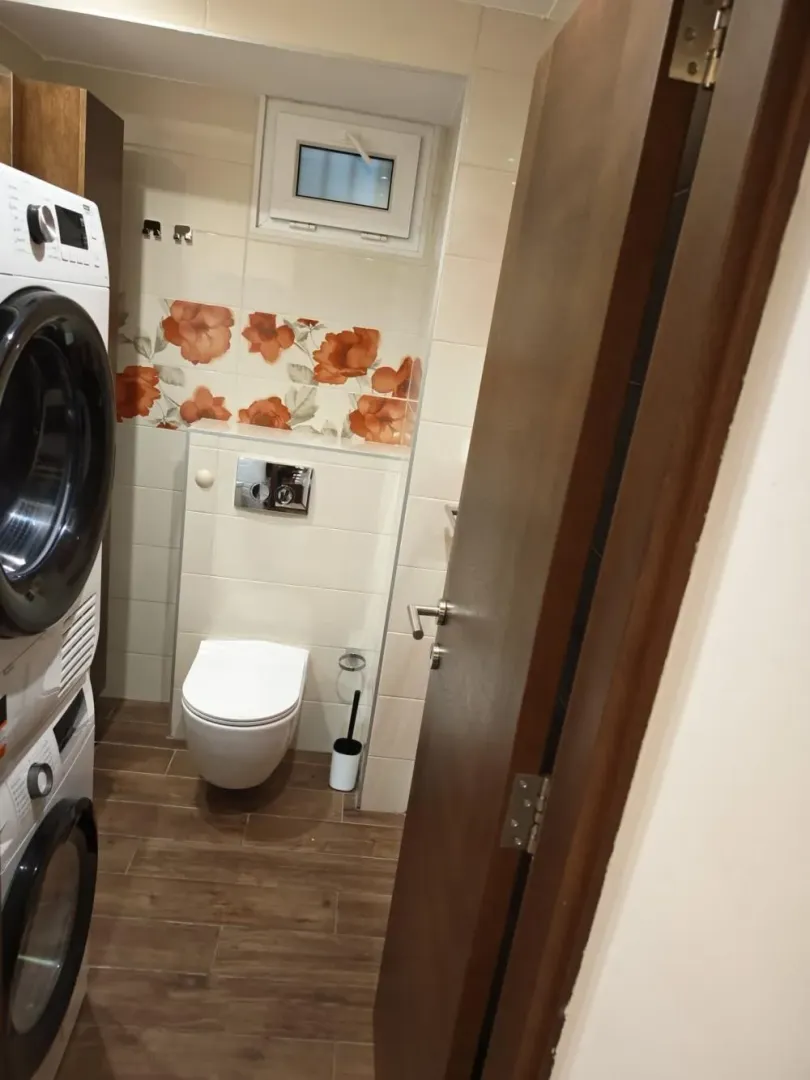 Kupatilo sa wc šoljom, prozorom i veš mašinom.