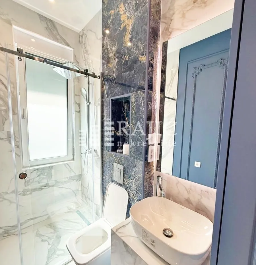 Modernly equipped bathroom with a shower cabin, washbasin, and marble tiles.