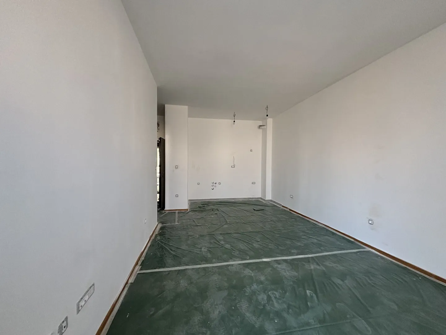 Prazna prostorija sa bijelim zidovima i podom prekrivenom zaštitnom folijom.