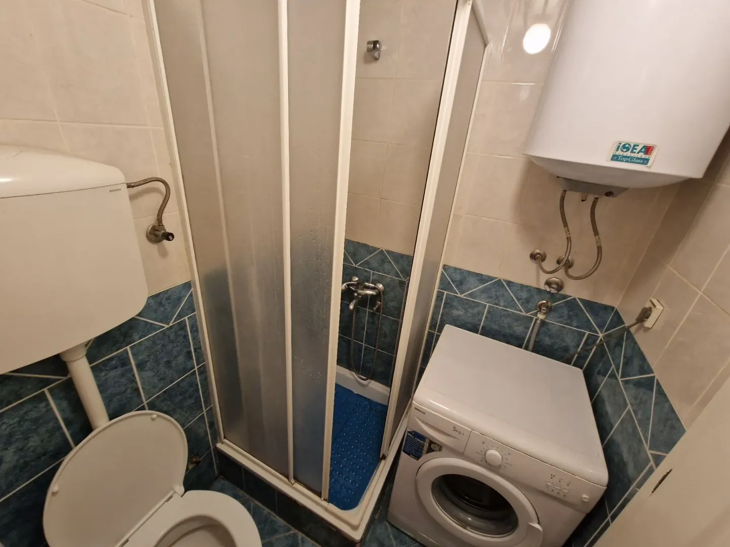 Bathroom with a shower cabin, toilet, washing machine, and water heater.