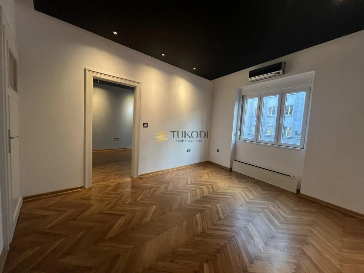 Empty room with wooden parquet flooring, white walls and a black ceiling.