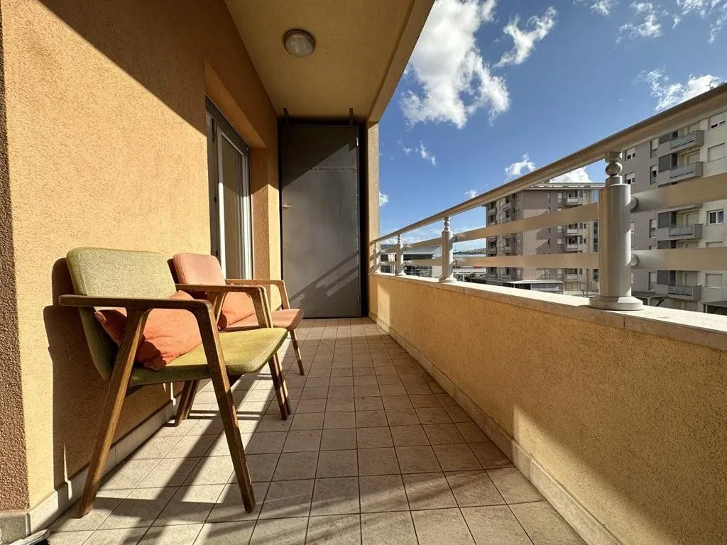 Natkriveni balkon sa stolicama i pogledom na okolne zgrade.