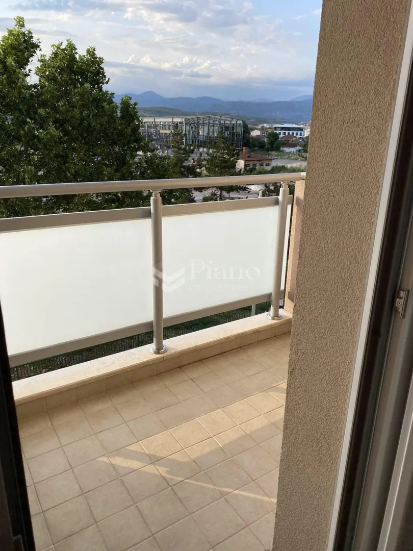 Manji popločani balkon sa metalnom ogradom i pogledom na grad i brda.