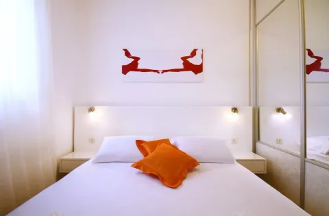 Bright bedroom with a double bed, white linens, and orange pillows. - image 7