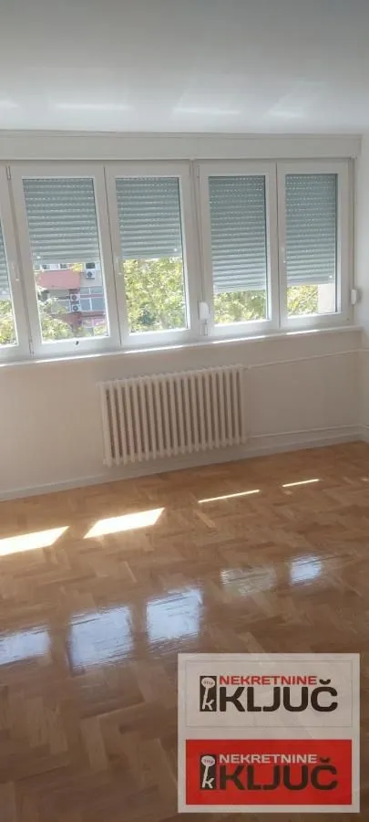 Prazna soba sa parketom i velikim prozorima.