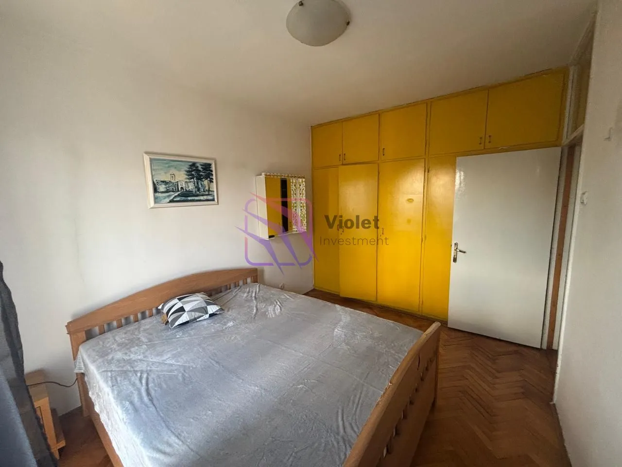 Bedroom with a double bed, large yellow wardrobe, and wooden parquet flooring.