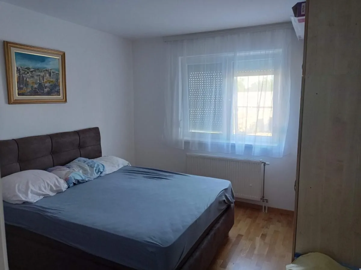Spavaća soba sa bračnim krevetom, prozorom i umetničkom slikom na zidu.