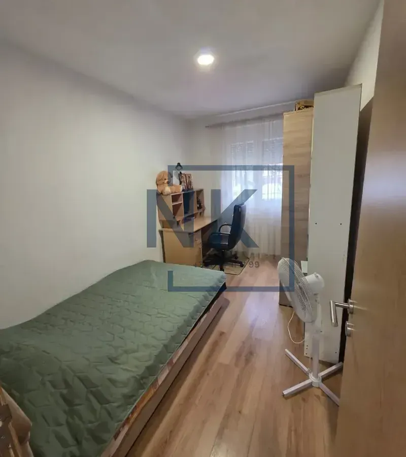 Manja spavaća soba sa krevetom, radnim stolom i ormarom.