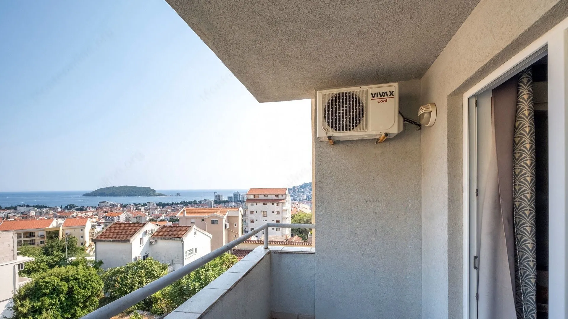 Natkriveni balkon sa klima-uređajem i pogledom na grad i more.