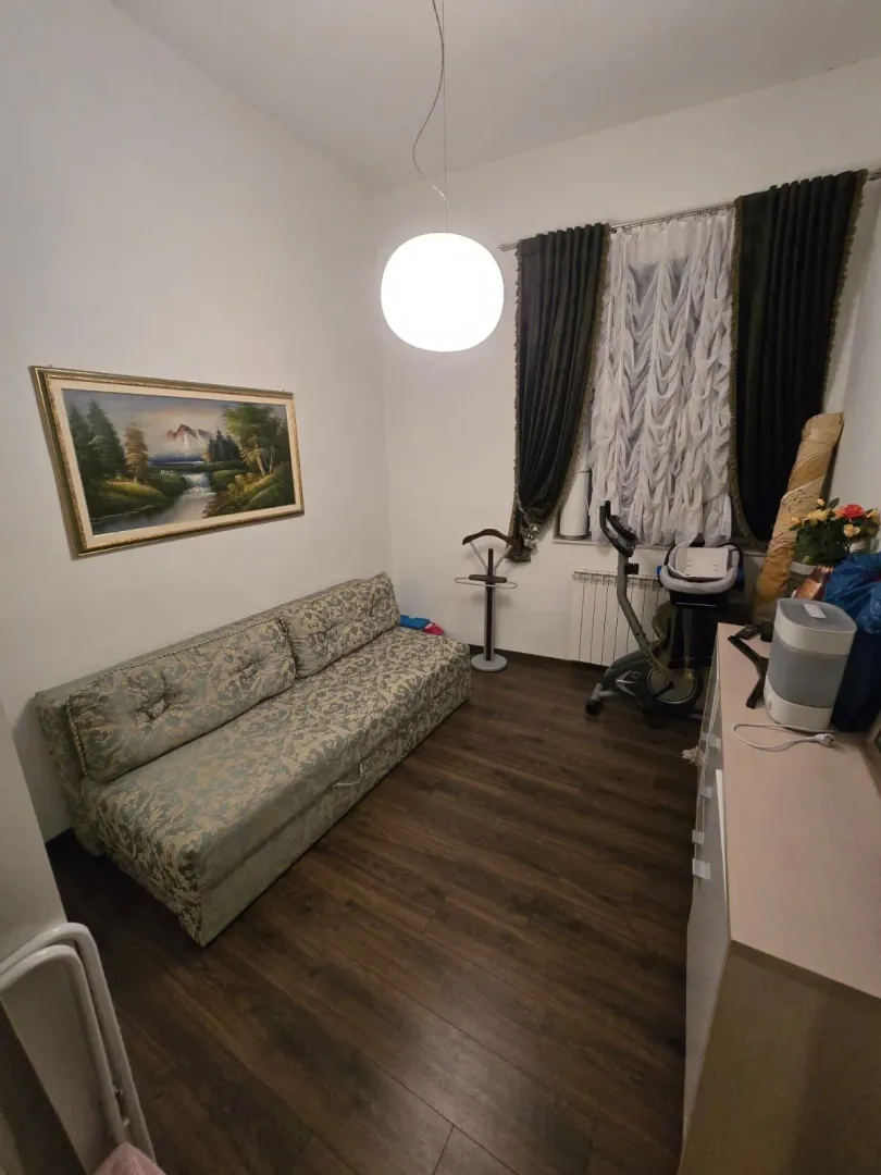 Dnevna soba sa kaučem, umjetničkom slikom na zidu i prozorom sa tamnim zavjesama.