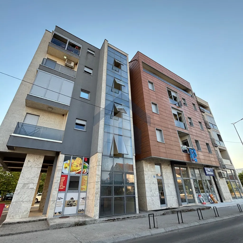 View of the exterior of a modern residential and commercial building with a balcony and ground floor retail space.