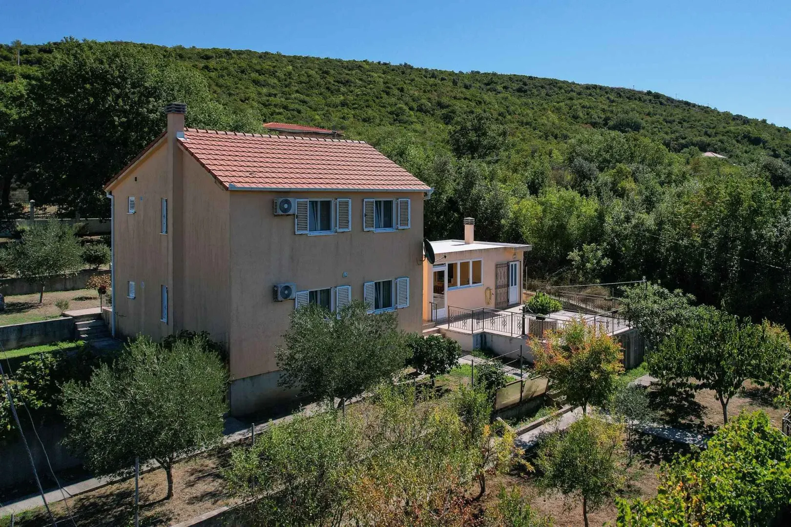 Pogled iz vazduha na porodičnu kuću sa uređenim dvorištem okruženom zelenilom.