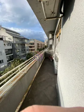 Dugačak spoljni balkon sa metalnom ogradom i pogledom na okolne zgrade. - image 11