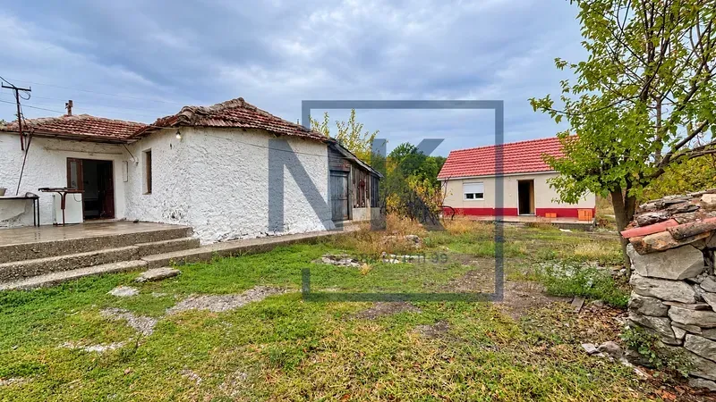 Pogled na dvorište i starije kuće sa pomoćnim objektom i zelenilom.