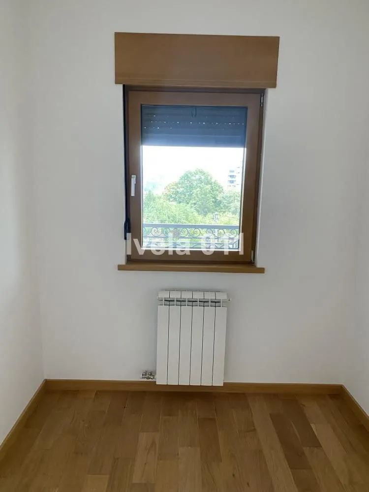 Prazna soba sa drvenim podom, prozorom i radijatorom.