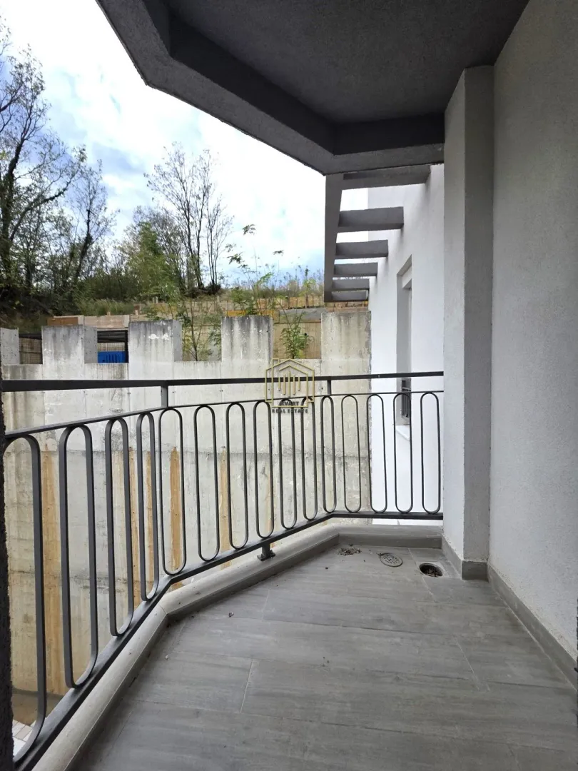Nenamješten balkon sa metalnom ogradom i pogledom na spoljašnjost.