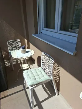 A balcony with a small round table and two white chairs with cushions. - image 10