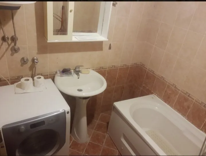 Jednostavno kupatilo sa kadom, lavaboom i veš mašinom.