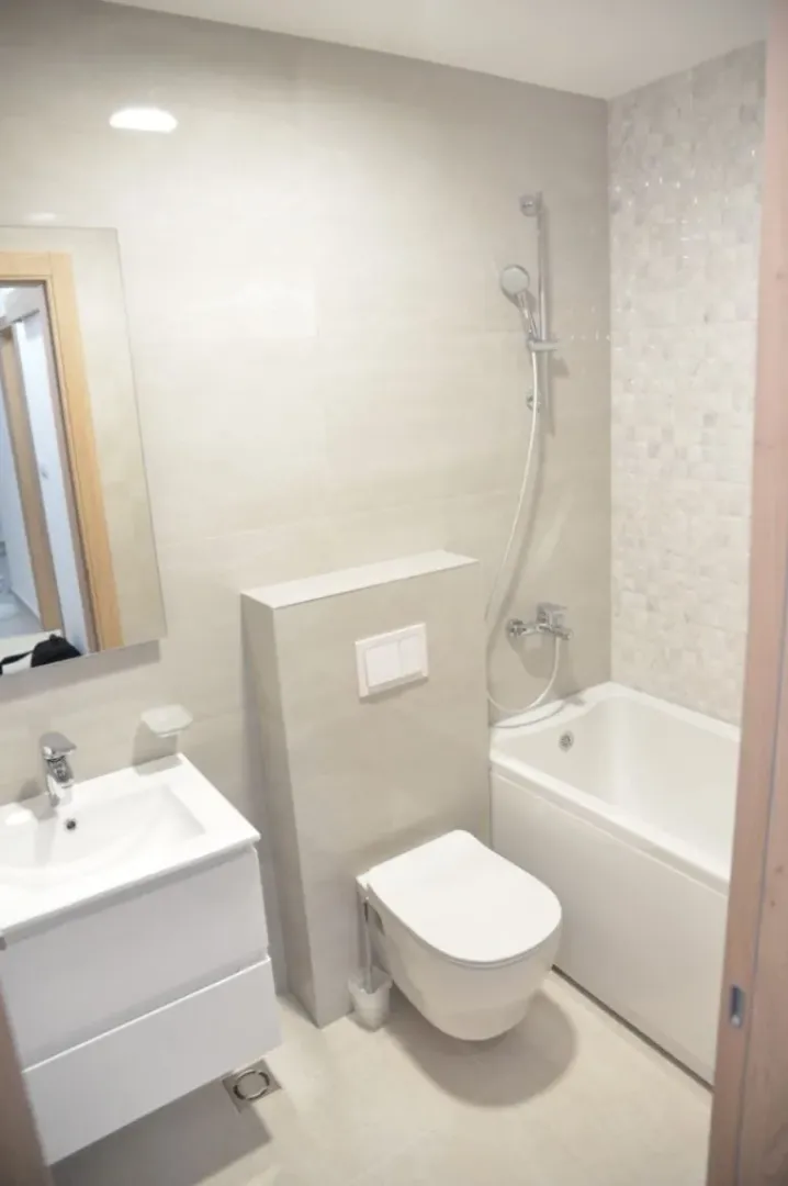 Modern bathroom with a bathtub, toilet, and sink in light tones.