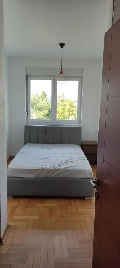 Spavaća soba sa bračnim krevetom, drvenim parketom i prozorom sa pogledom.