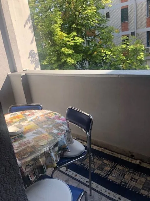Nameštena terasa sa stolom, stolicama i pogledom na zelenilo.