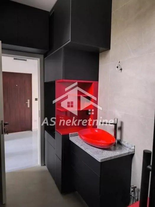 Moderna kuhinja sa crnim elementima i crvenim detaljima.