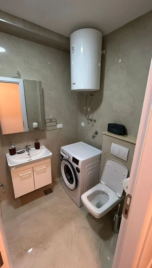 Small bathroom with a sink, toilet, washing machine, and water heater.