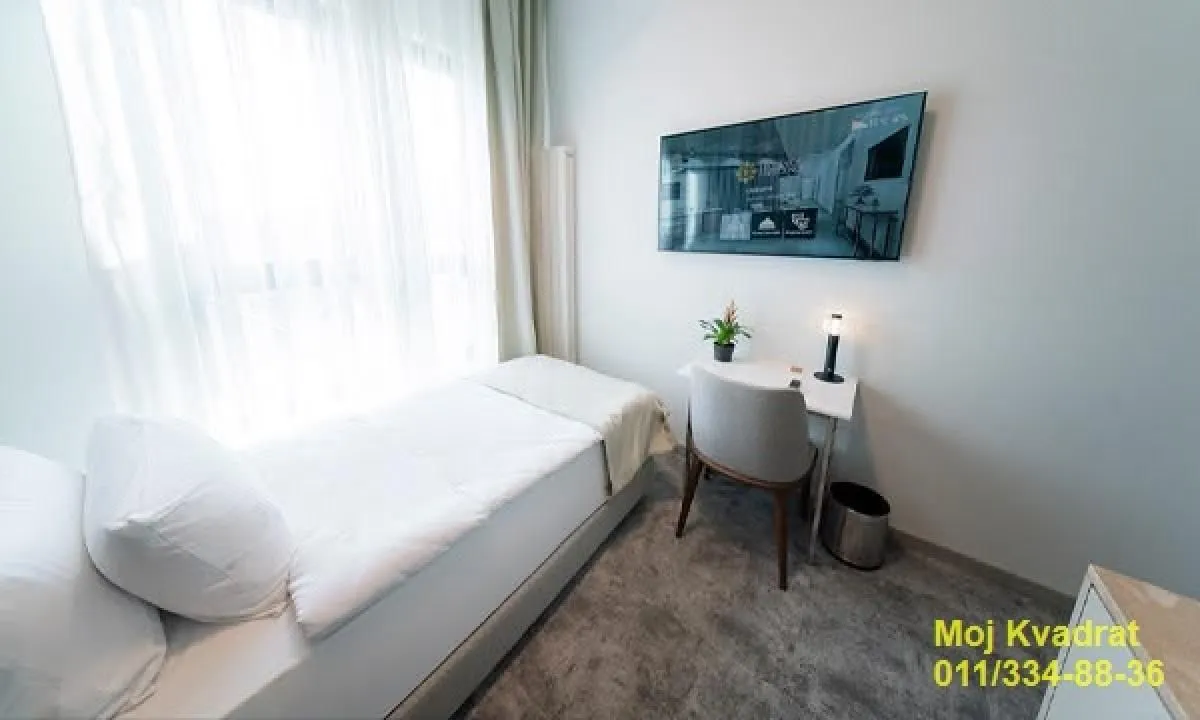 Small bedroom with a bed, a desk, and a wall-mounted TV.
