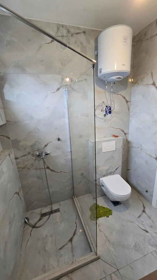 Moderne kupatilo sa tuš kabinom obloženom staklenim paravanom i ugrađenom wc šoljom.