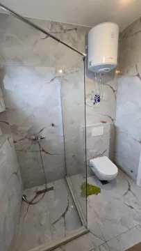 Moderne kupatilo sa tuš kabinom obloženom staklenim paravanom i ugrađenom wc šoljom. - image 8