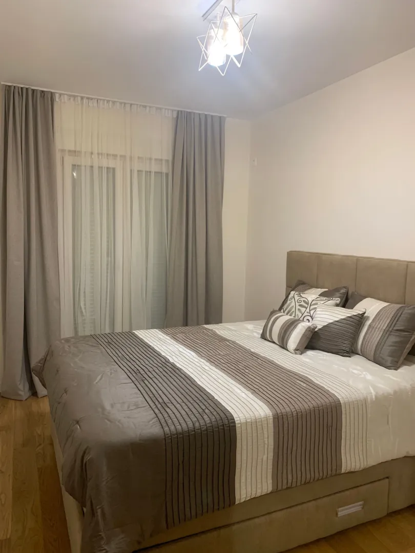 Furnished bedroom with a double bed and a window with curtains.