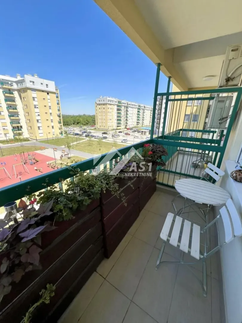 Namešten balkon sa garniturom za sedenje i pogledom na naselje.