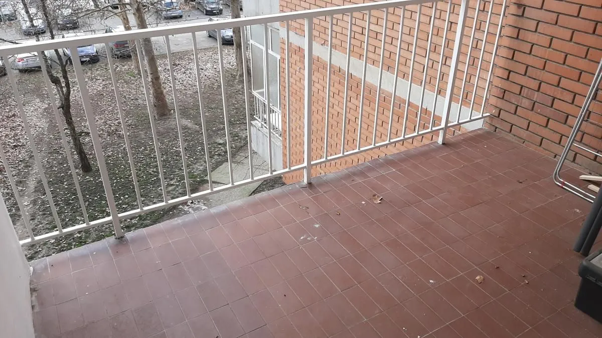 Manji popločani balkon sa belom ogradom i pogledom na dvorište.