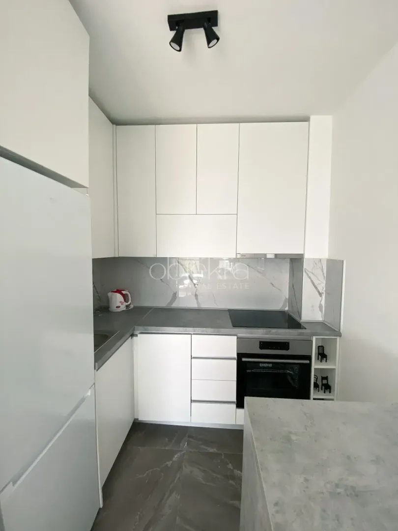 Modern white kitchen with gray countertop and built-in appliances.