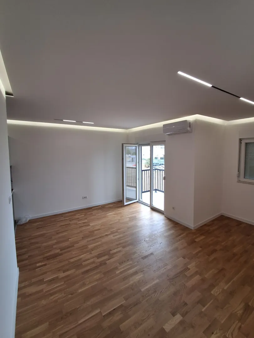 Empty bright room with wooden flooring, dropped ceiling and access to a balcony.