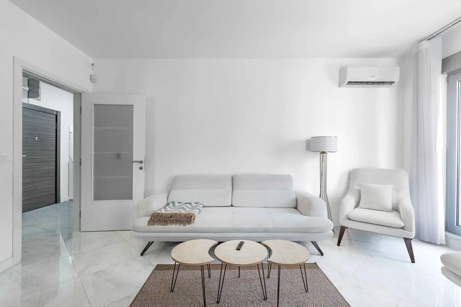 Bright living room with a white sofa, armchair, and modern coffee tables.