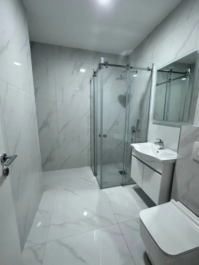 Modern bathroom equipped with a walk-in shower, washbasin, and white ceramic tiles.